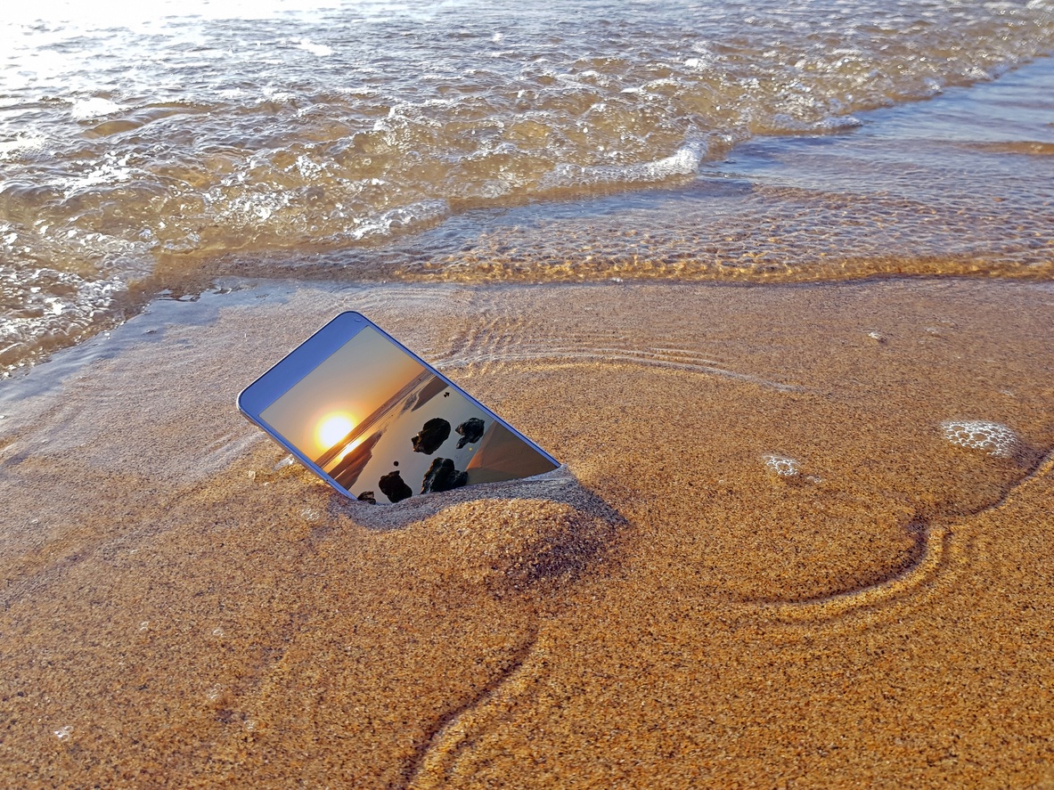 smartphone partly submerged in the sand and tide - a photo of the beach on its display screen