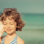 young girl closes her eyes and listens with a large seashell to her ear