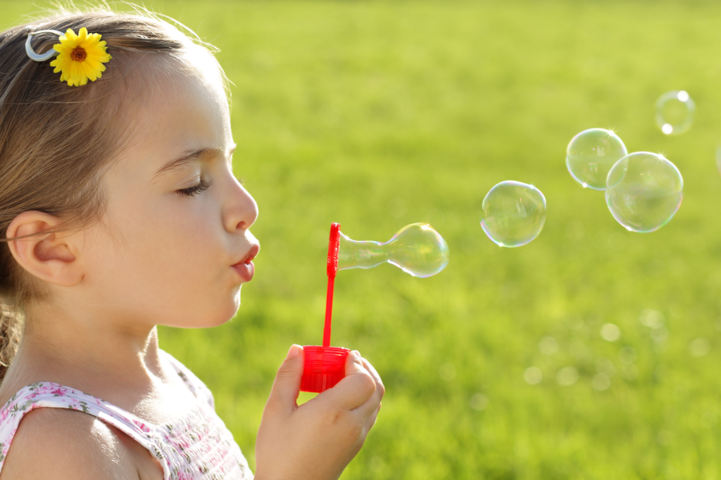 creating space - little girl closes eyes and blows bubbles across the green grass