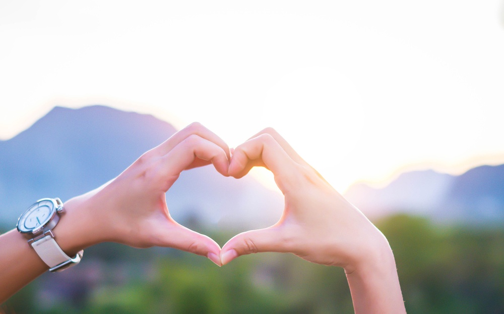 God pursues you with unrelenting love - human weakness and God's love - a girl's hands form heart shape against a background of sky