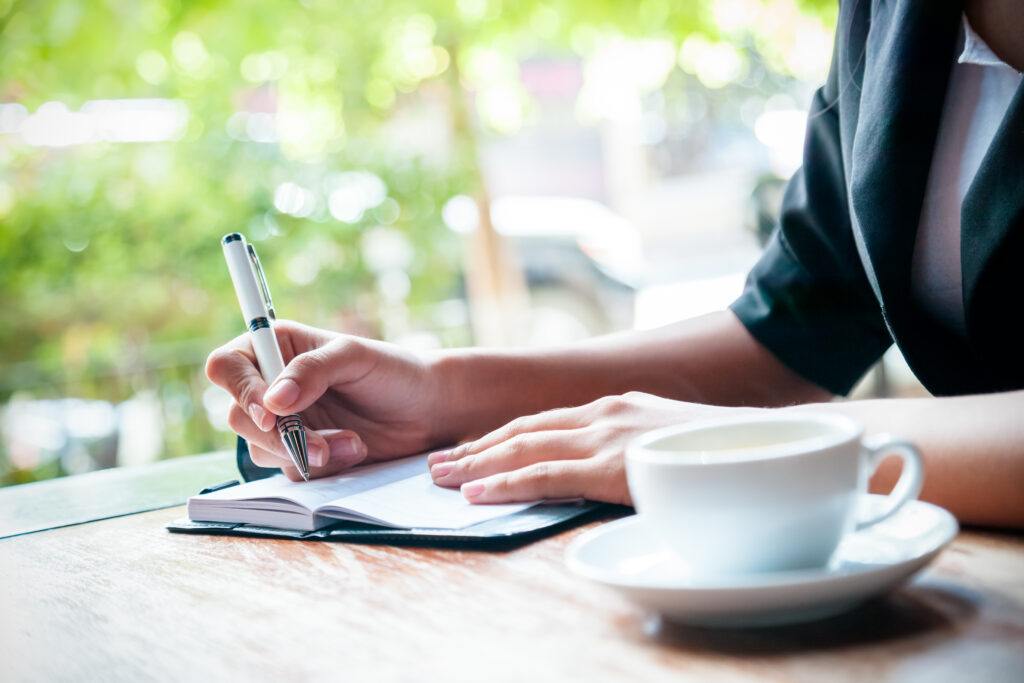 How to Start a Daily Mindfulness Journal - a woman writing in her journal and a cup of coffee sits next to her