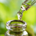 detail of glass eye dropper dispensing one drop of essential oil into a glass bottle