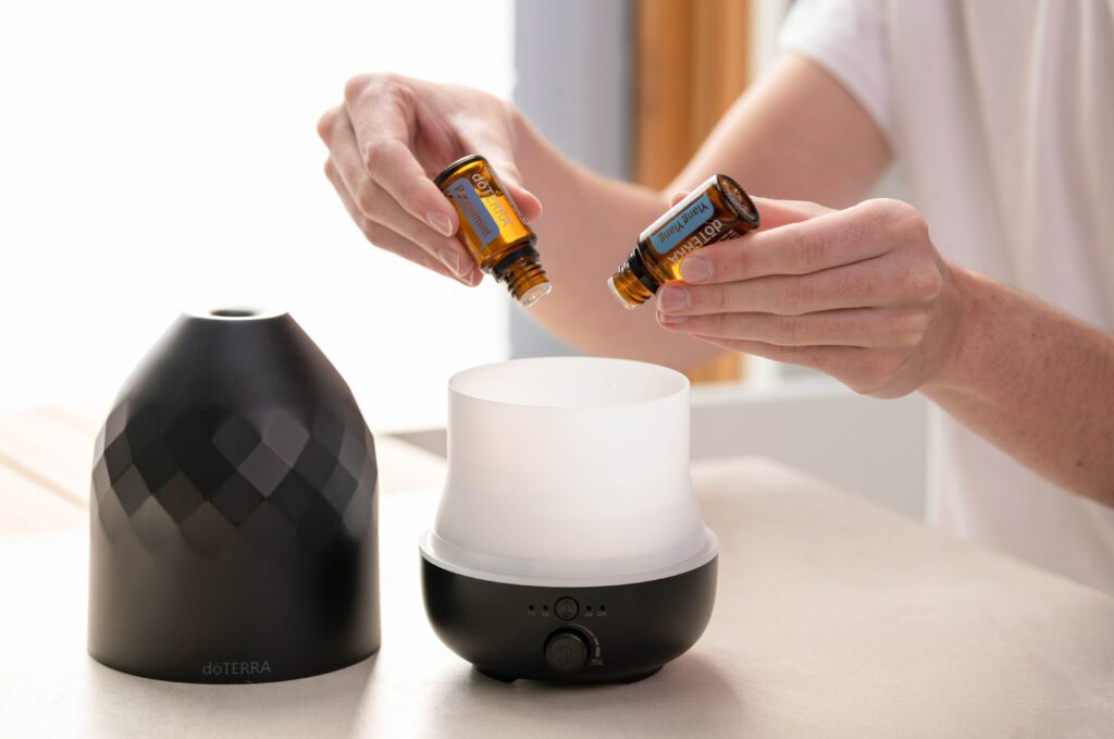 a woman adds drops of essential oil to a diffuser for aromatherapy