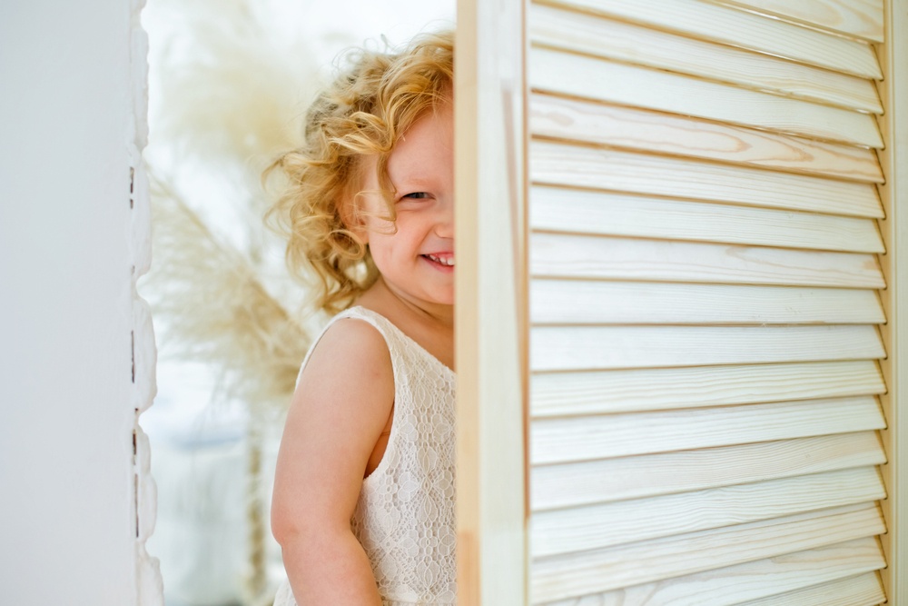 Where Is Your Hiding Place - little girl hiding behind screen giggling - Shutterstock