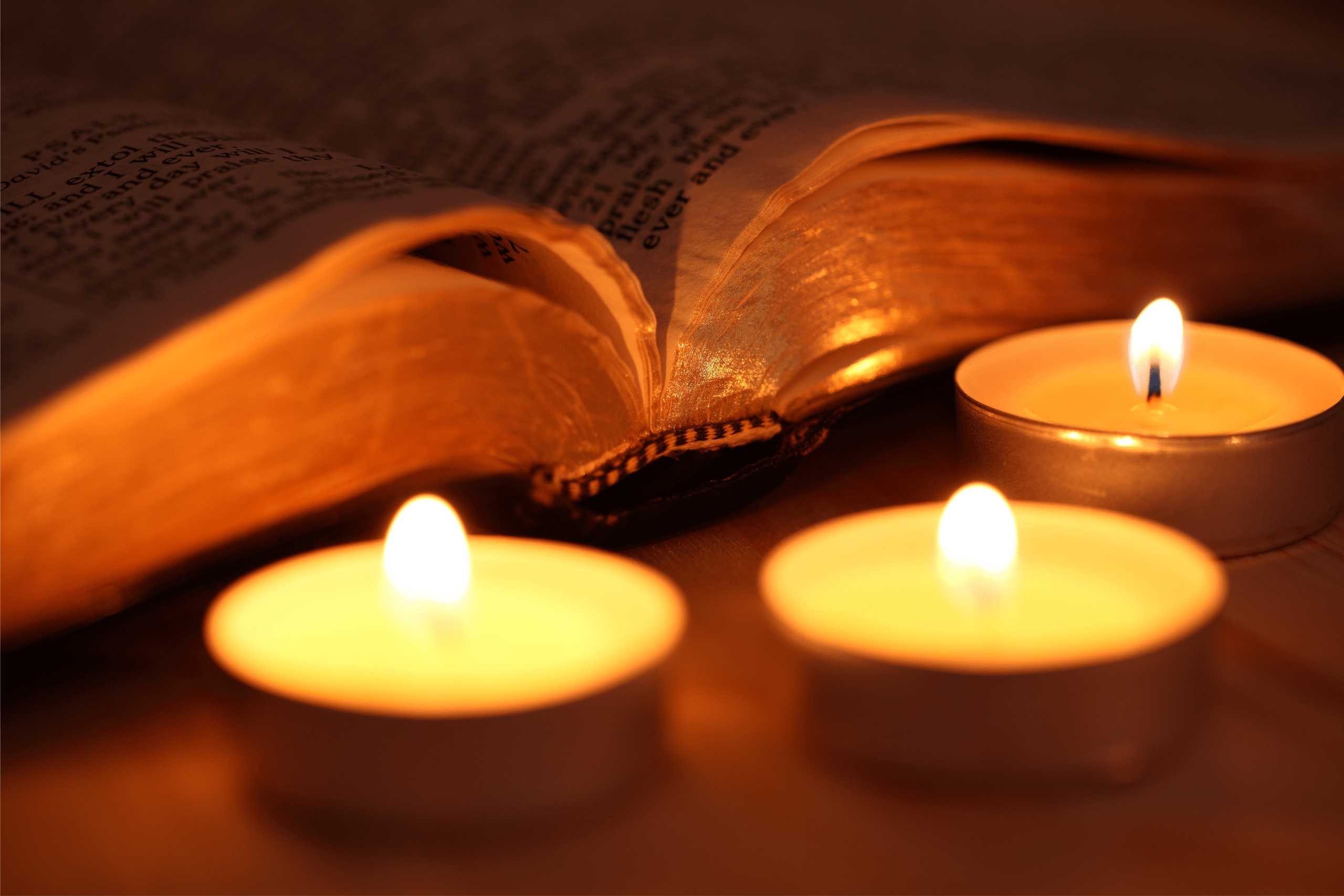 three tea light candles flicker sitting next to an open Bible