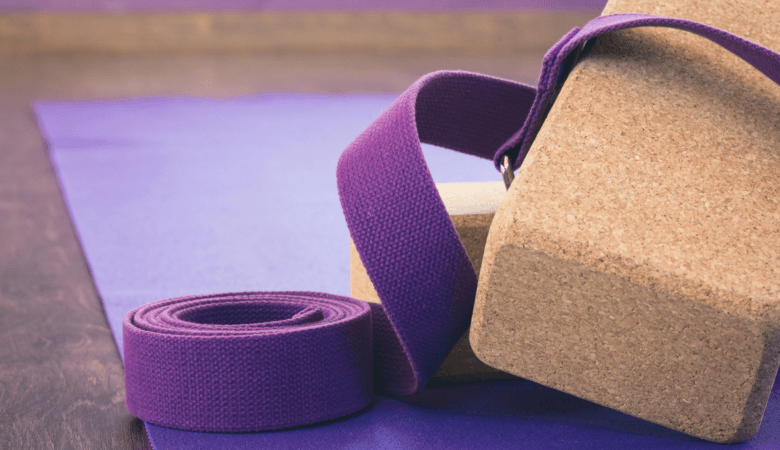 two cork blocks and a purple yoga strap sit on a purple yoga mat