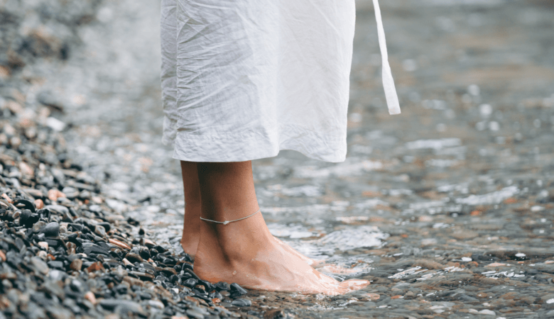 a woman's bare feet standing on river rocks as the stream washes against her toes