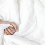 What are the most comfortable sheets? White bed sheets gripped by a sleepy hand.