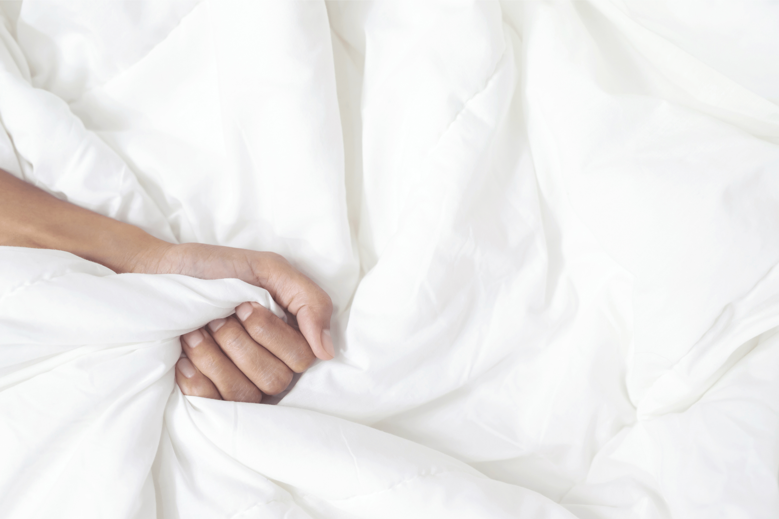 What are the most comfortable sheets? White bed sheets gripped by a sleepy hand.