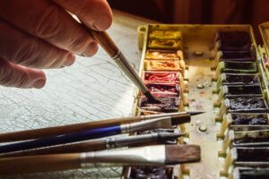 man's hand on paint brush - mixing tubes of color on palette