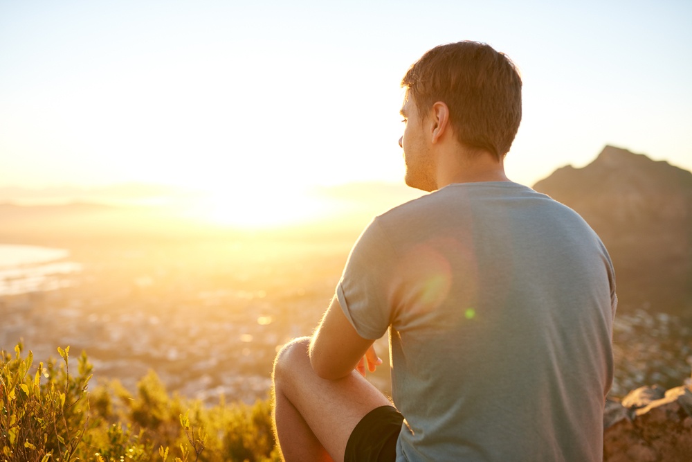 the old and the new - god leads you into a new land - young man sits on mountain top gazing to the forest below - Shutterstock