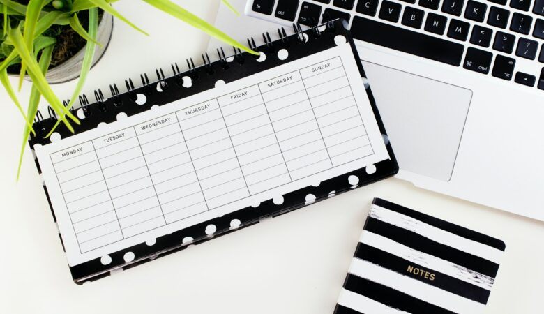 A weekly planner lies open next to a notebook and keyboard
