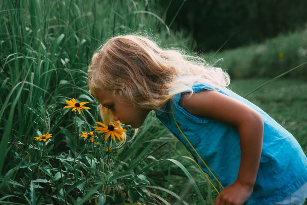 Your Sense of Smell - Blonde little girl in blue dress smelling a yellow flower