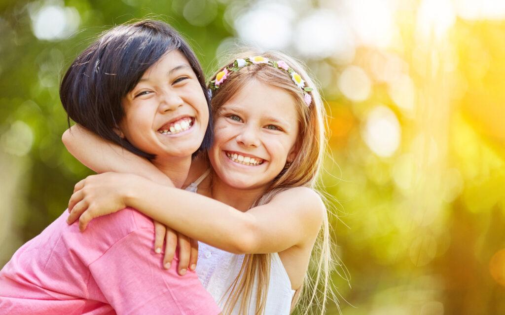 two young girls hugging with big smiles outdoors