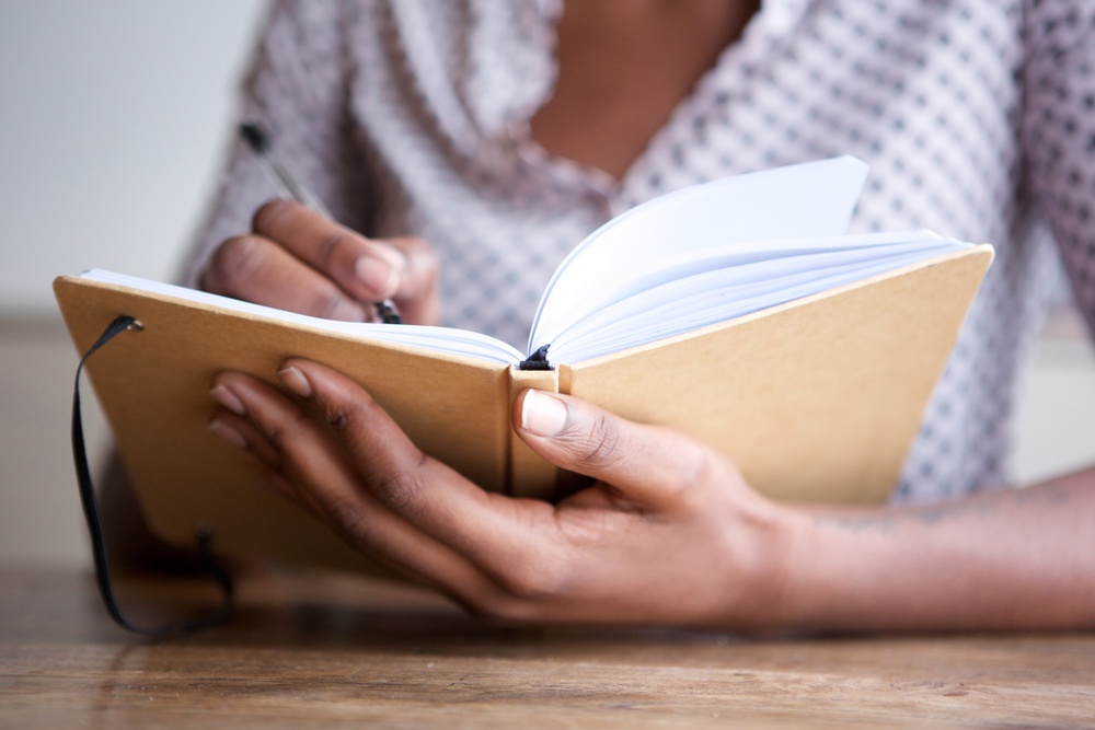 Journaling is good for relaxation and stress relief - hands of a woman writing in journal - Shutterstock