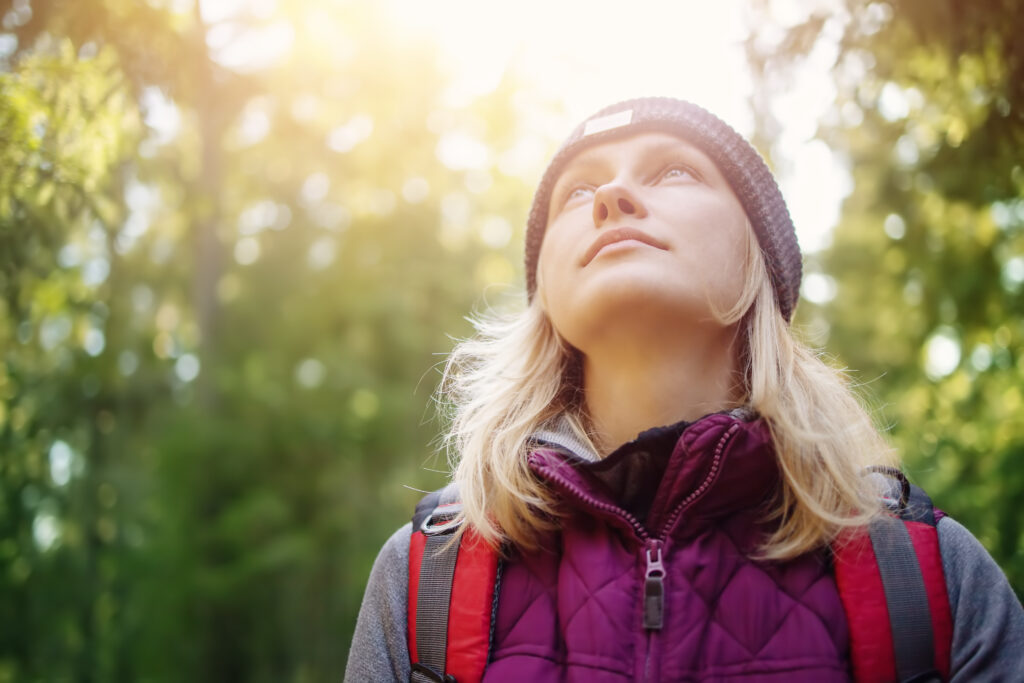 young woman in fall clothing looks up at trees - in awe of God and the wonder of creation - spiritual aspects of forest bathing