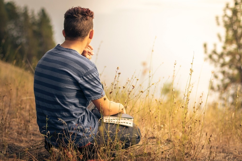 man sitting in field praying - seeking God in sadness - photo by Timothy Eberly - Unsplash